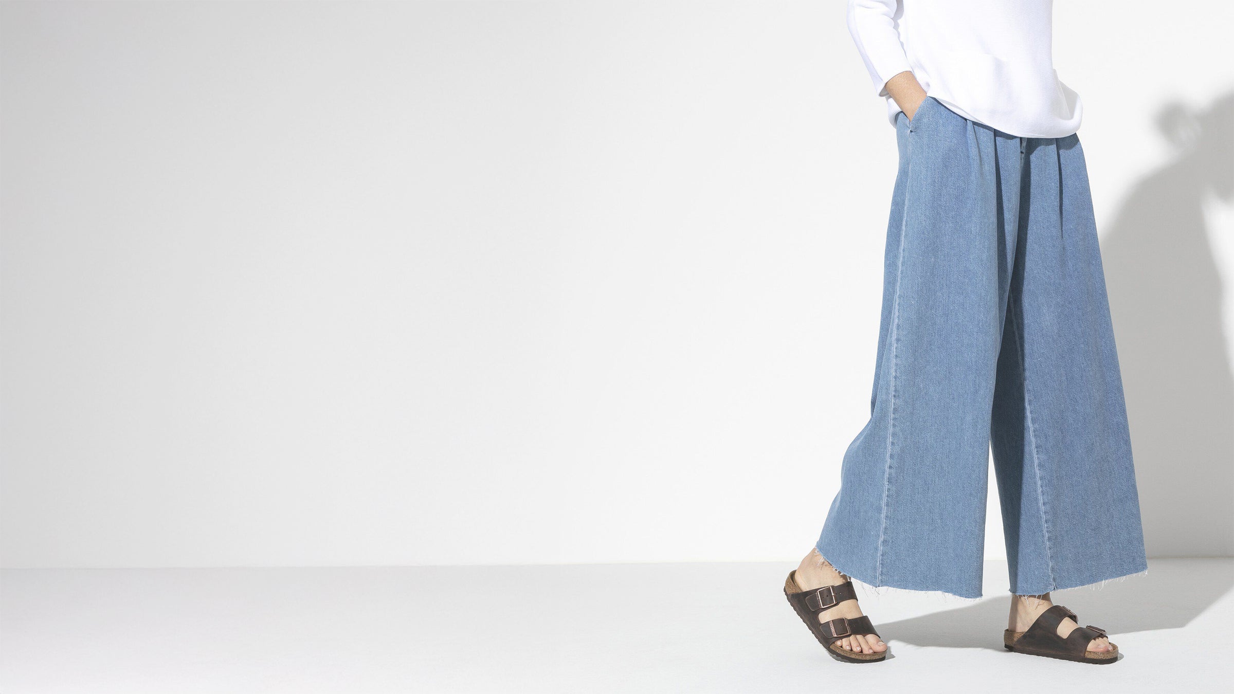 Person wearing light blue wide-leg jeans and a white shirt on a plain background