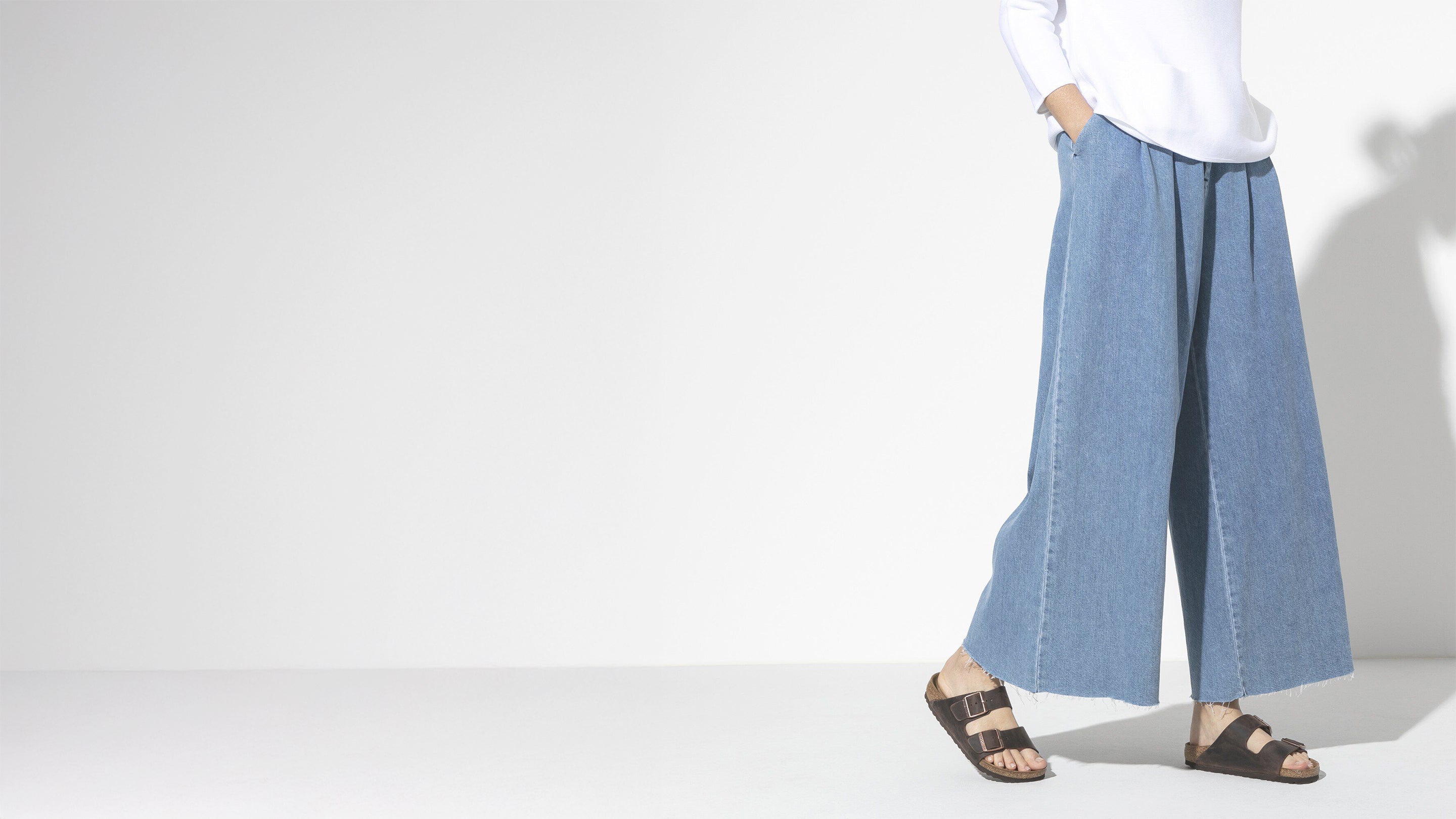 Person wearing light blue wide-leg jeans and a white shirt on a plain background