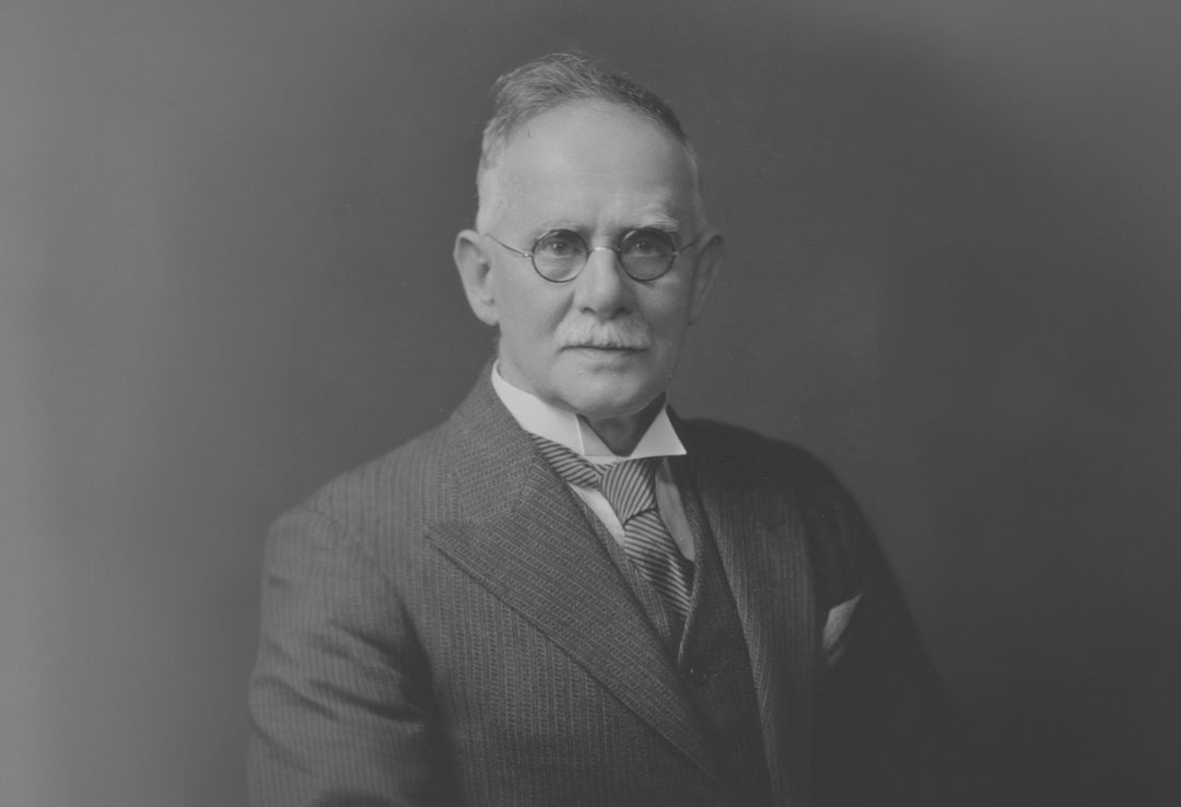 Black and white portrait of a man in formal attire with glasses against a dark background