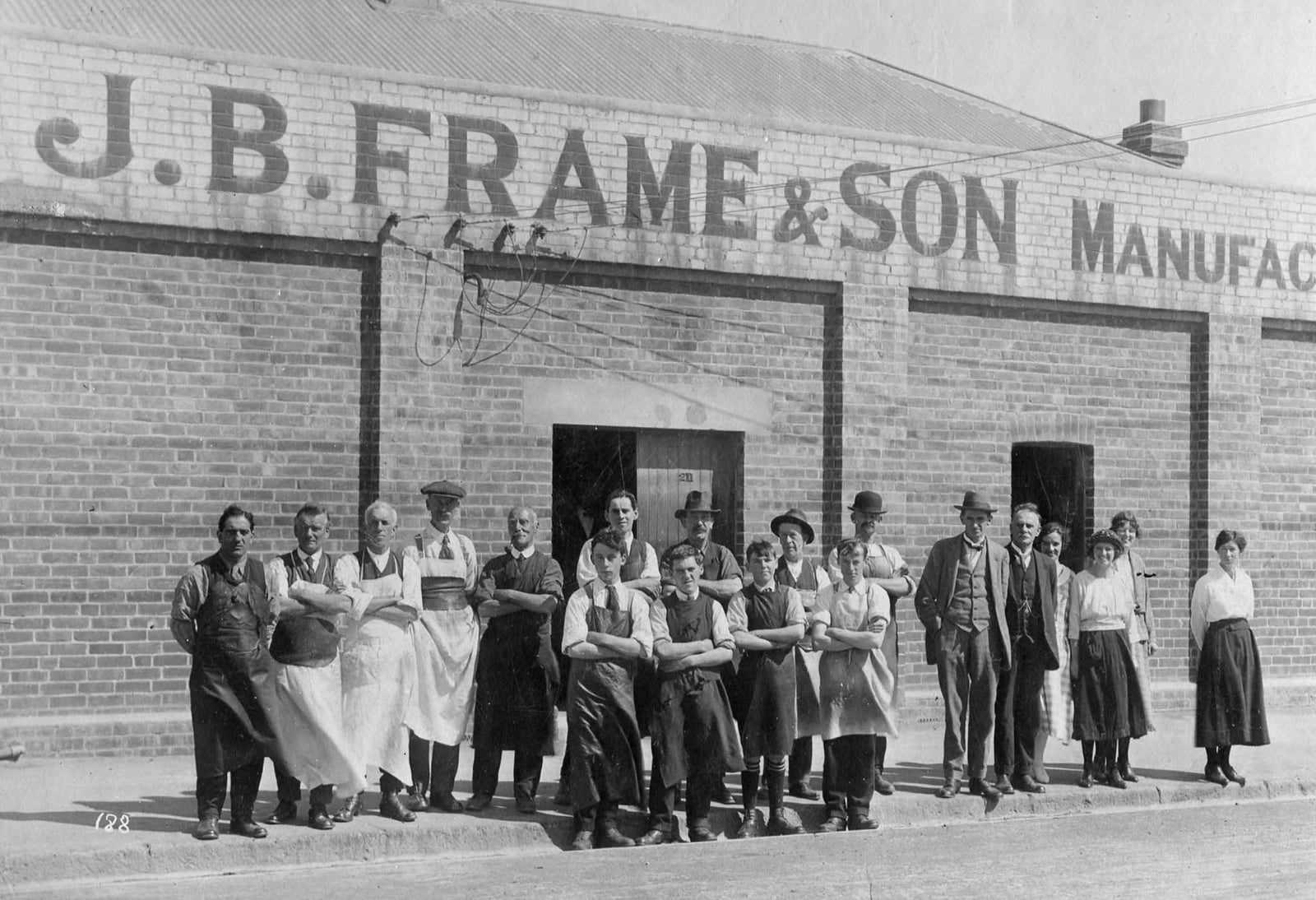 Black and white photograph of a group of people in front of a building with 'J.B. Frame & Son' signage.